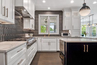 A kitchen with white cabinets , a stove , a sink , and a large island.
