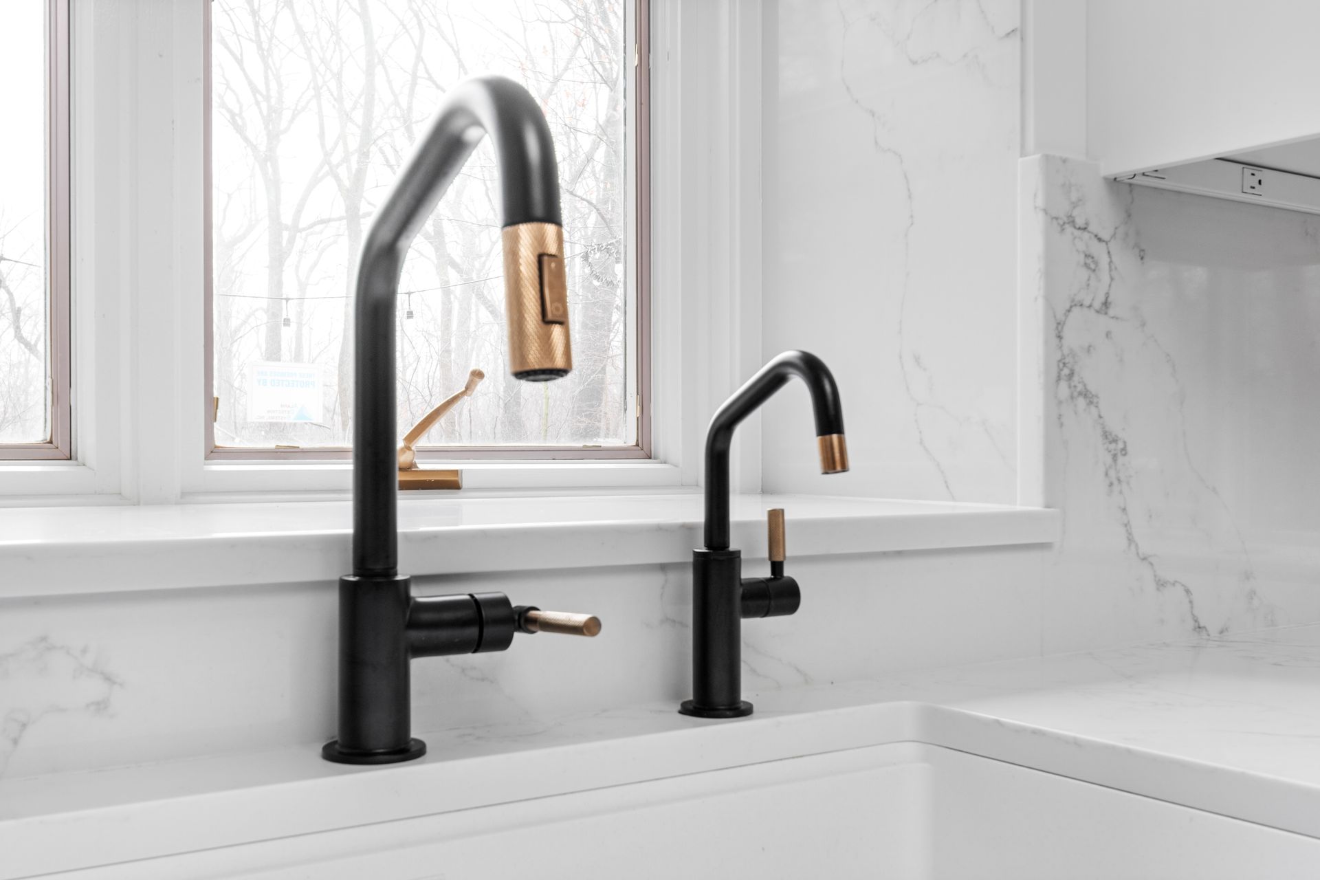 A kitchen sink with two black faucets and a window.