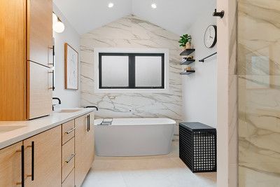 A bathroom with a tub , sink , mirror and window.