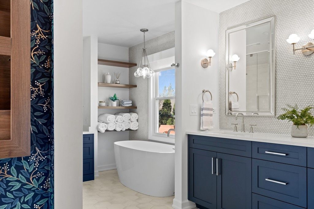 A bathroom with a bathtub , sink , mirror and blue cabinets.
