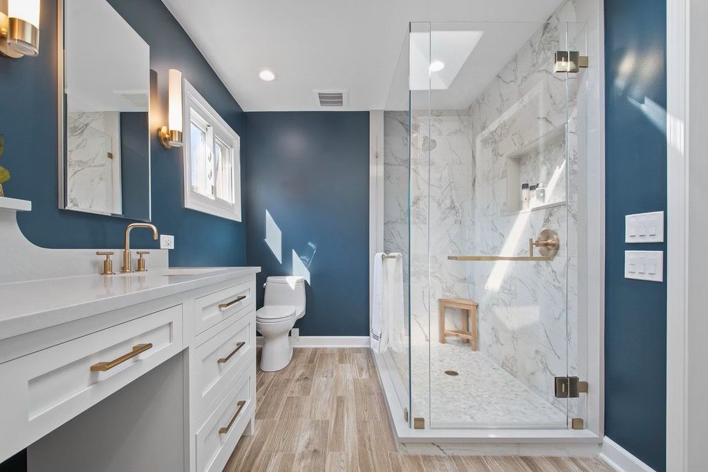 A bathroom with a toilet , sink , mirror and walk in shower.