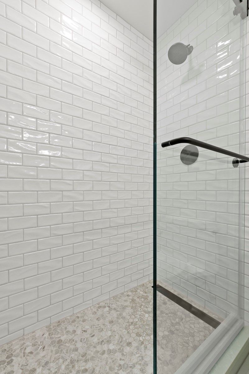 A walk in shower with white tiles and a glass door.