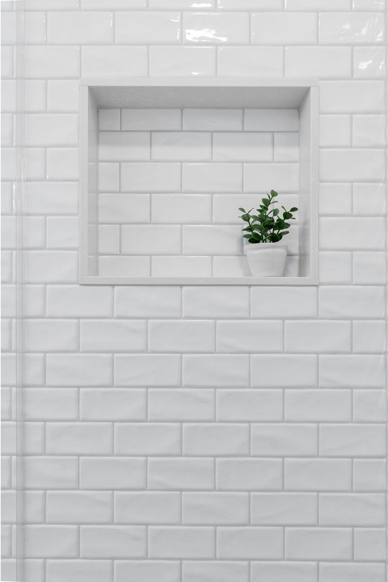 A white subway tile shower niche with a potted plant in it.