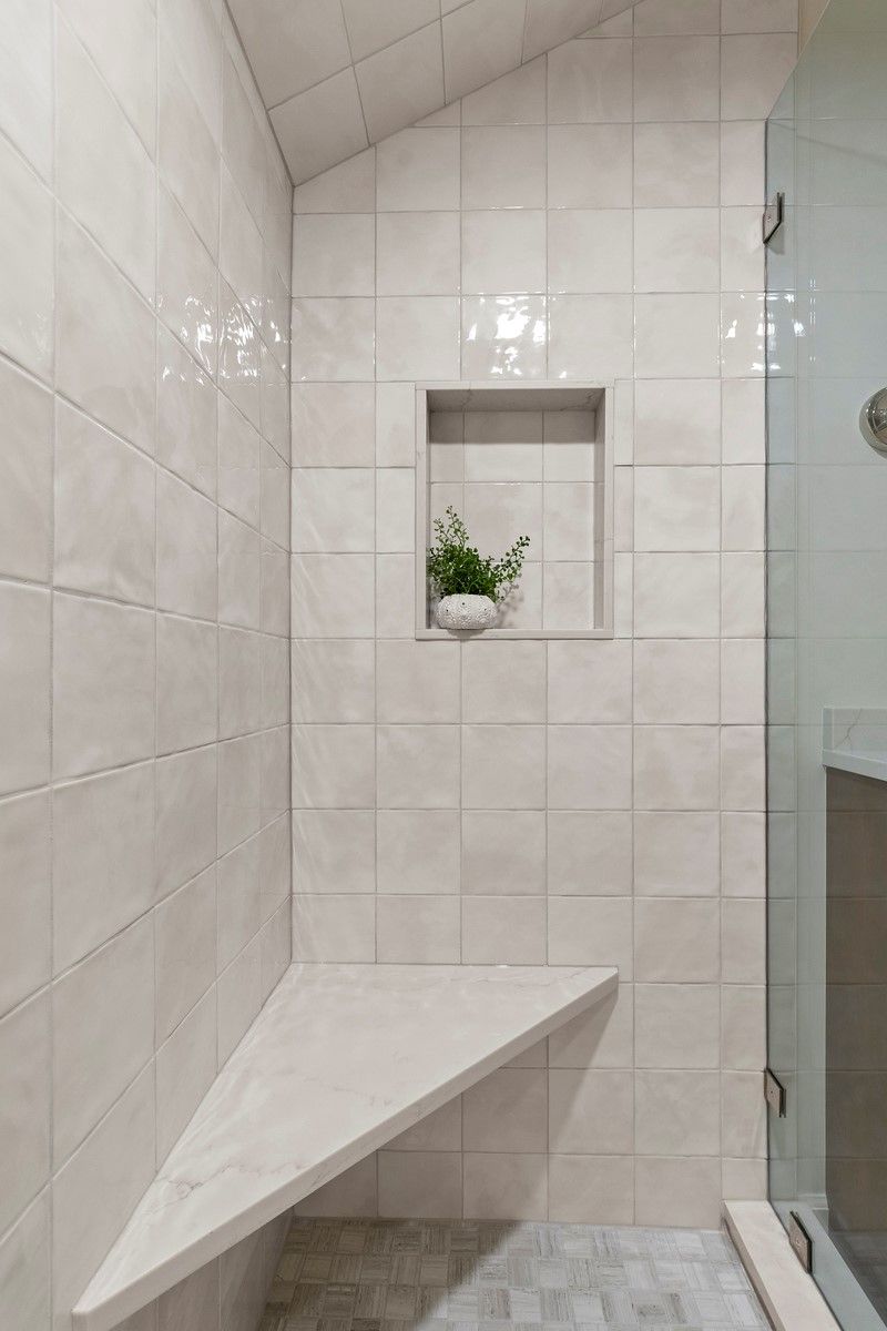 There is a bench in the shower with a plant in it.