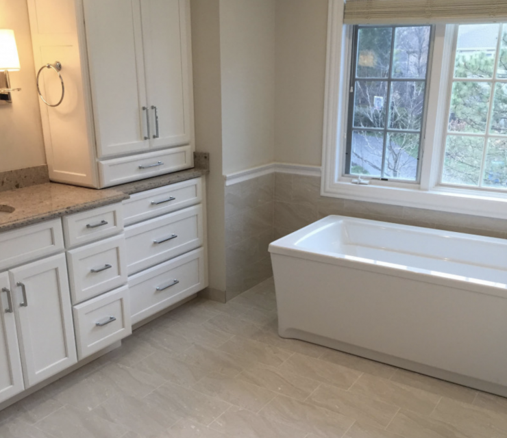 A bathroom with a tub , sink , cabinets and a window