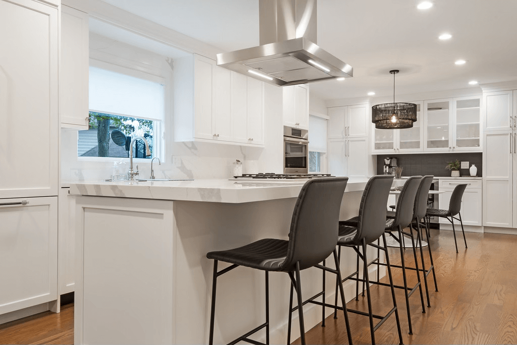A kitchen with white cabinets , stainless steel appliances , and a large island with stools.