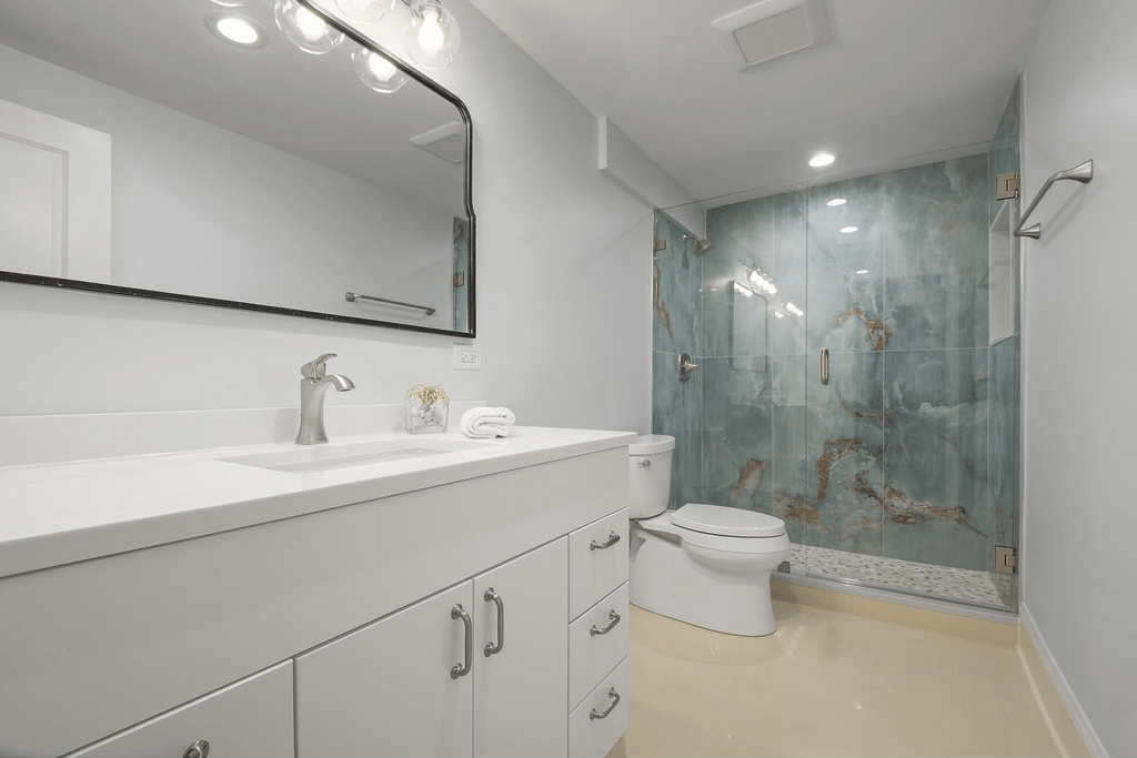 A bathroom with a toilet , sink , mirror and walk in shower.