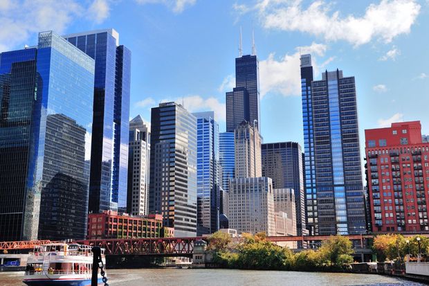 Skyline of modern high-rise buildings beside a river under a blue sky with clouds