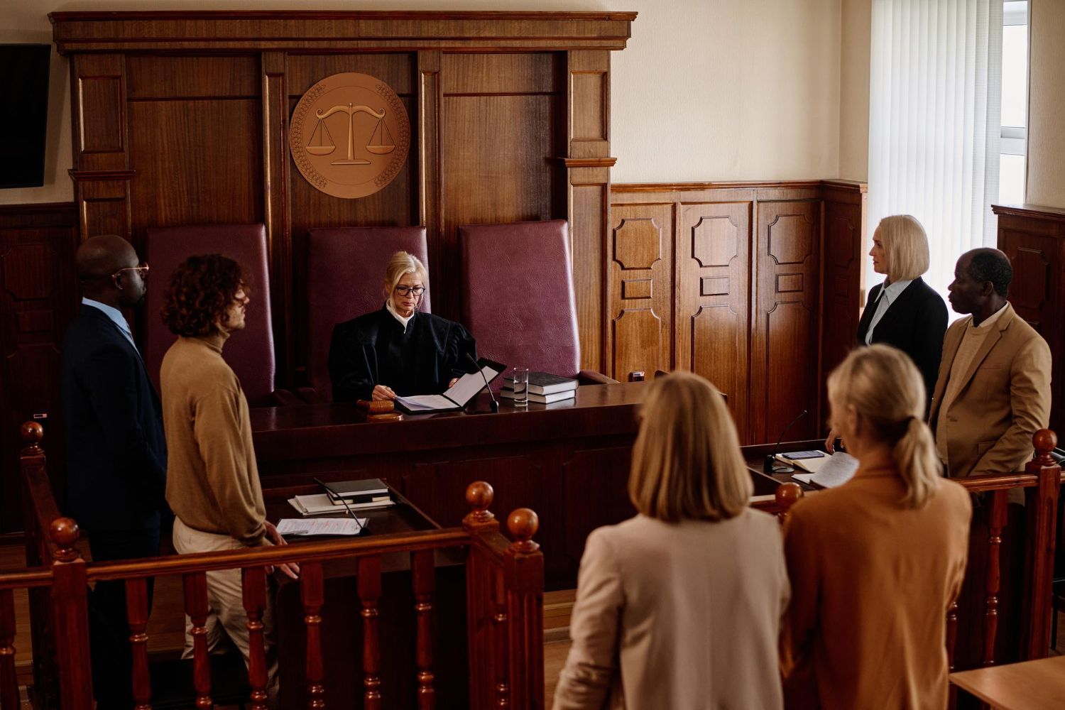 Courtroom scene with a judge at the bench and people standing in the gallery, facing forward.