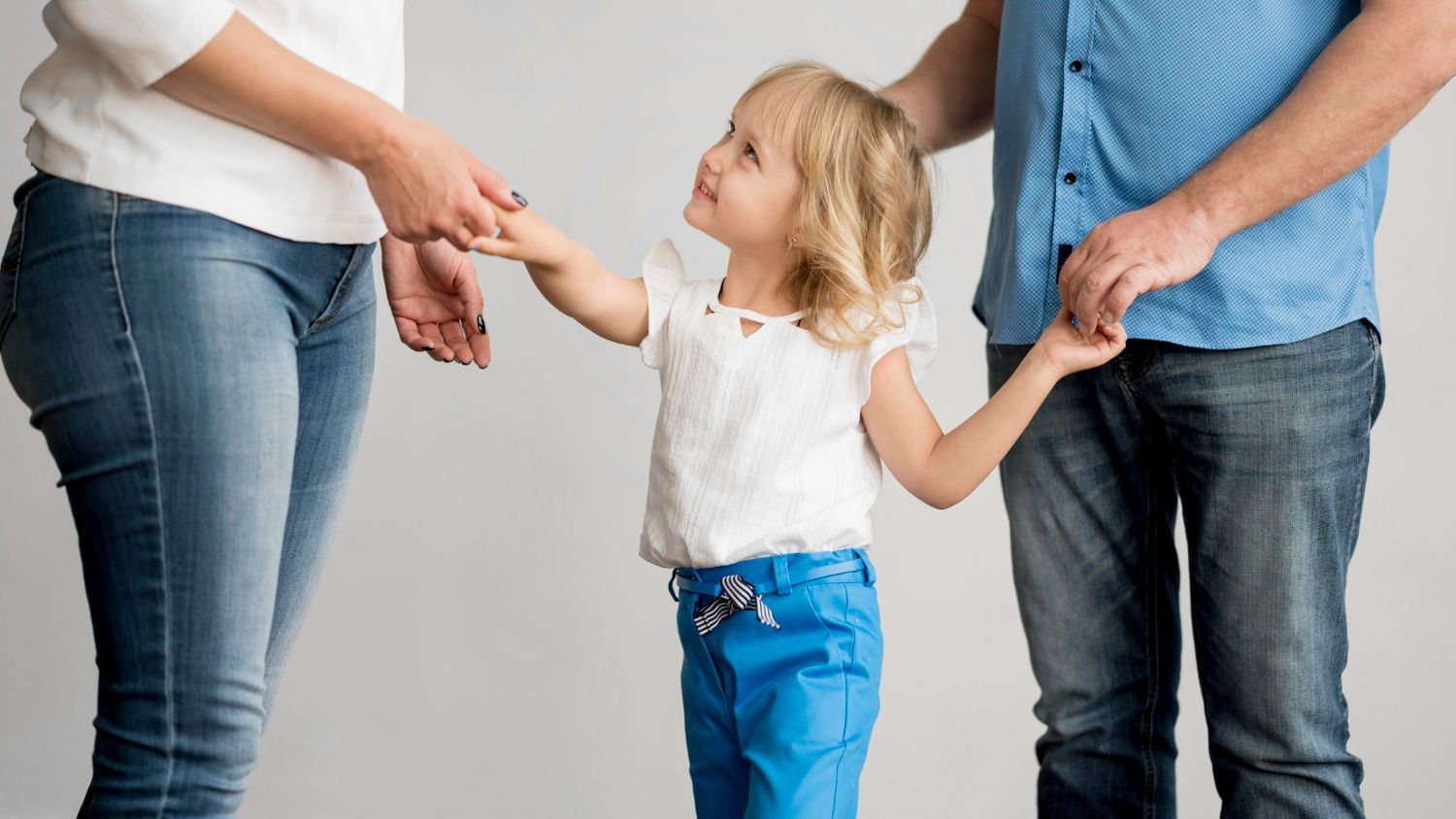 Adults holding a child's hands, standing together against a gray background
