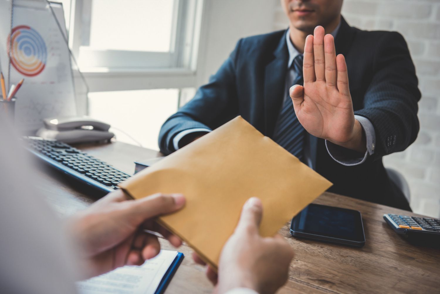 Person in a suit raises a hand to stop a document being handed over at a desk