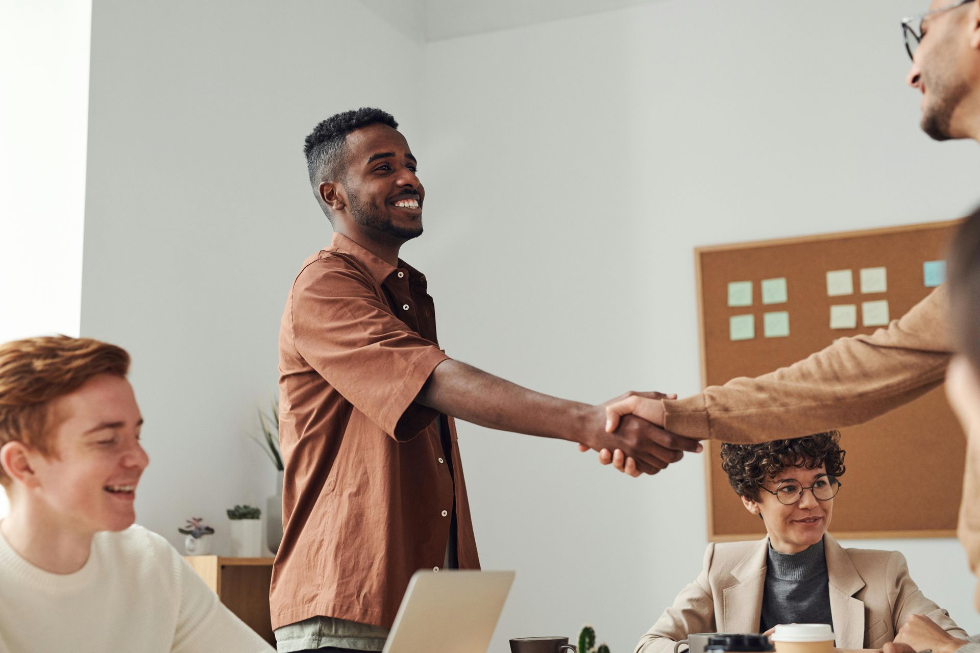 Two coworkers shaking hands across a conference table in a bright office meeting room