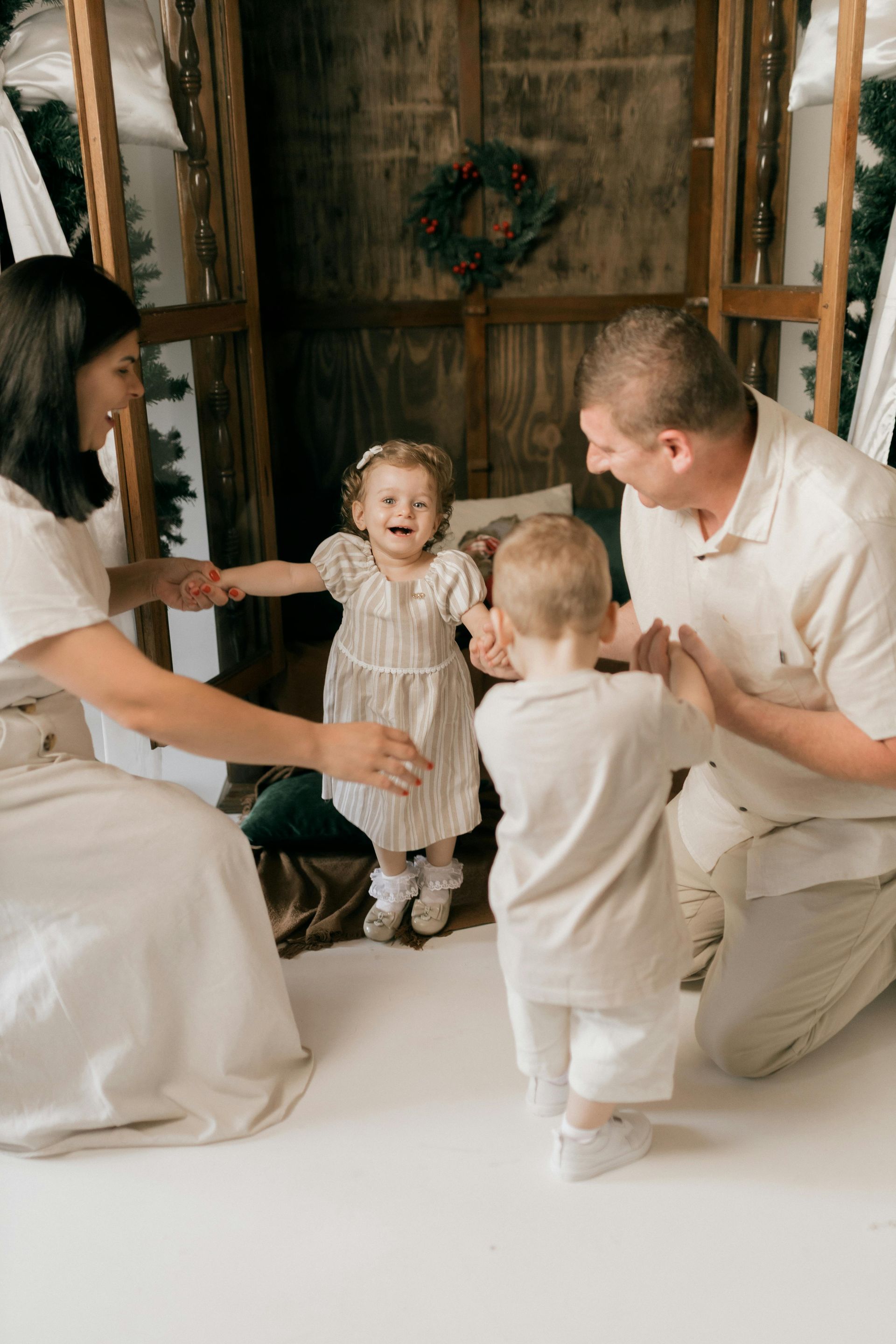 Family gathered in a rustic room, smiling and reaching toward a toddler in a white outfit