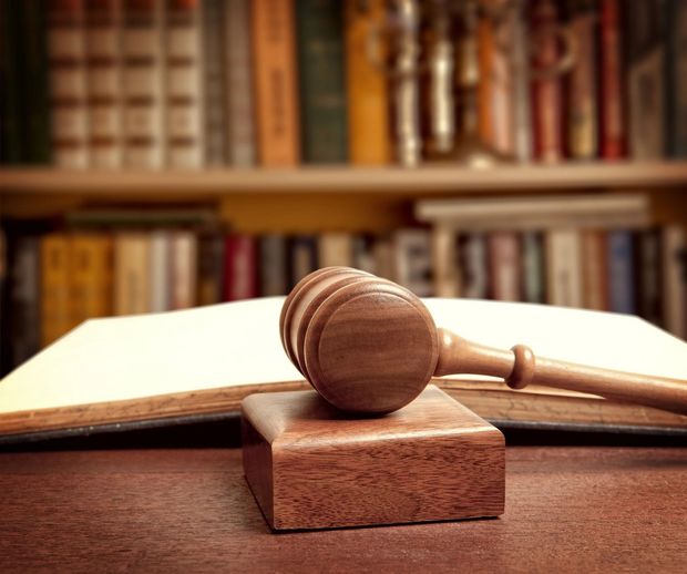Judge's gavel on a wooden block before an open book, with blurred bookshelves in the background.
