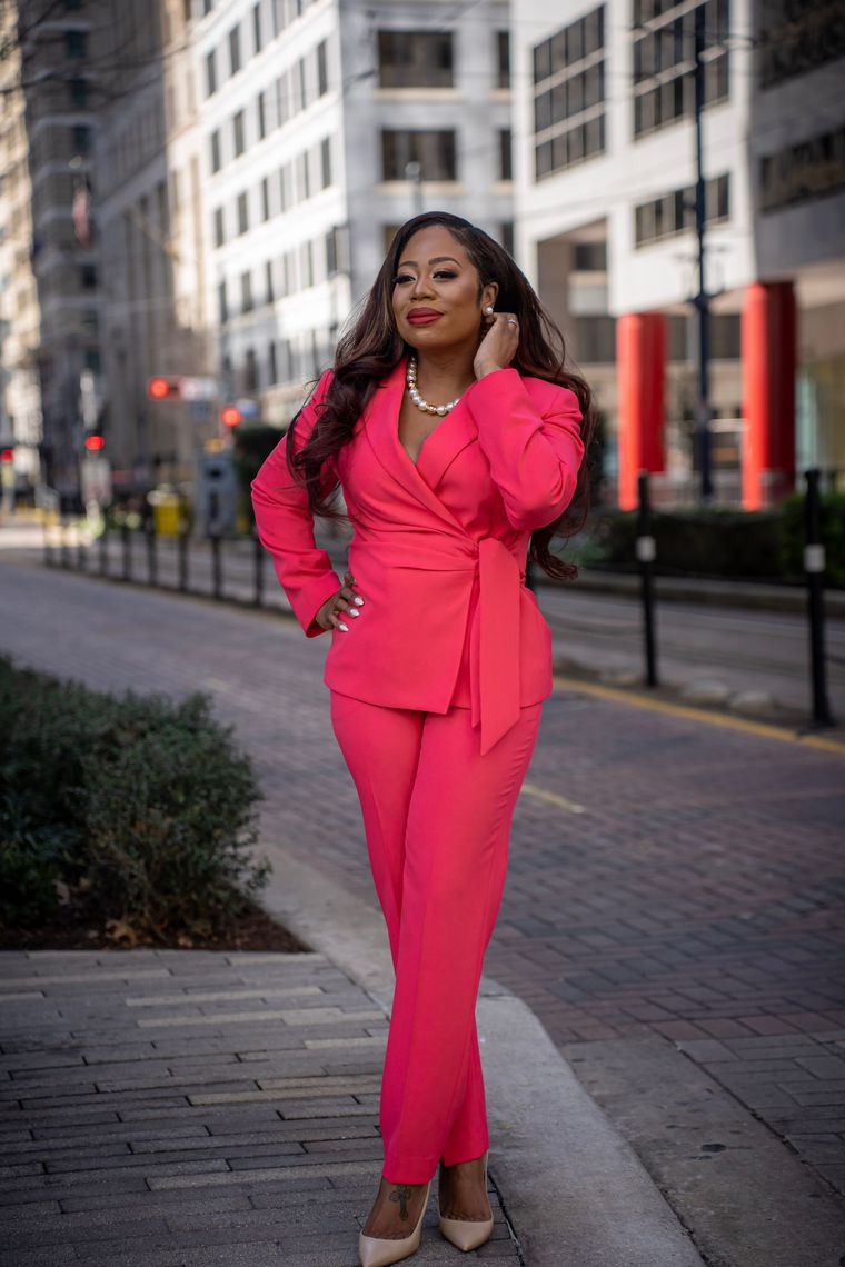 a woman in a pink suit is standing on a sidewalk in front of a building .