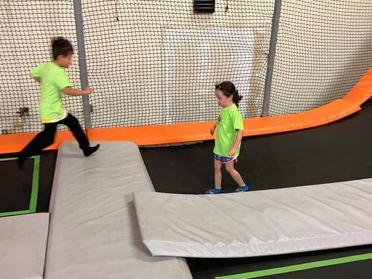 A boy and a girl are playing on a trampoline.