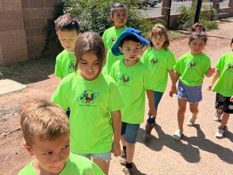 A group of children wearing neon green shirts are walking down a dirt road.
