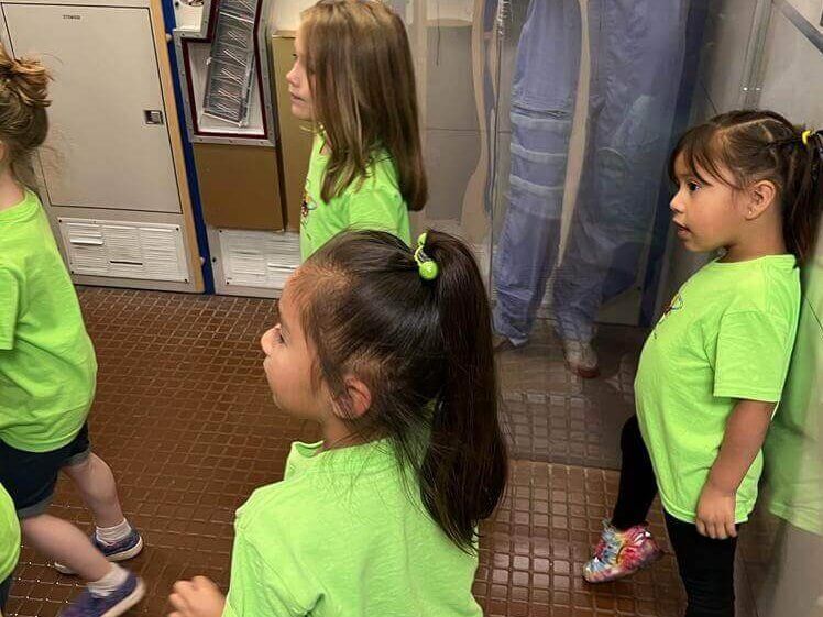 A group of young girls in green shirts are standing next to each other in a bathroom.