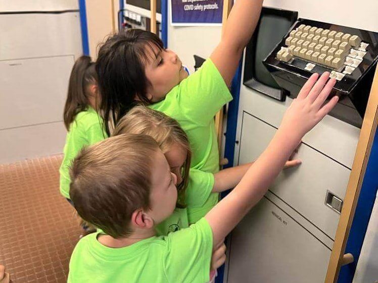 A group of children in green shirts are reaching for a keyboard