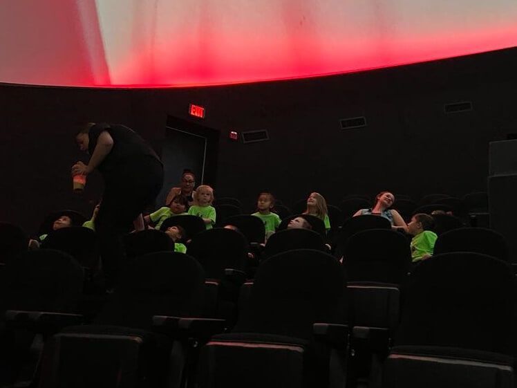 A group of people are sitting in a dark room with a red light on the ceiling.
