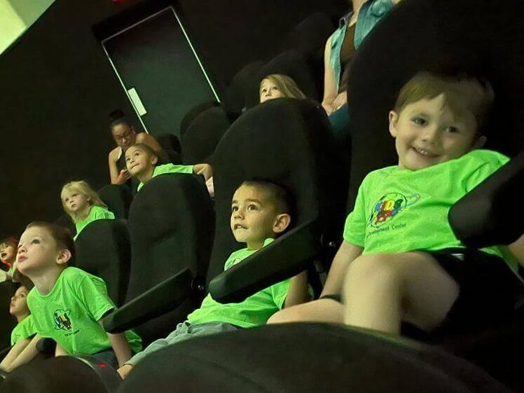 A group of children in green shirts are sitting in black chairs