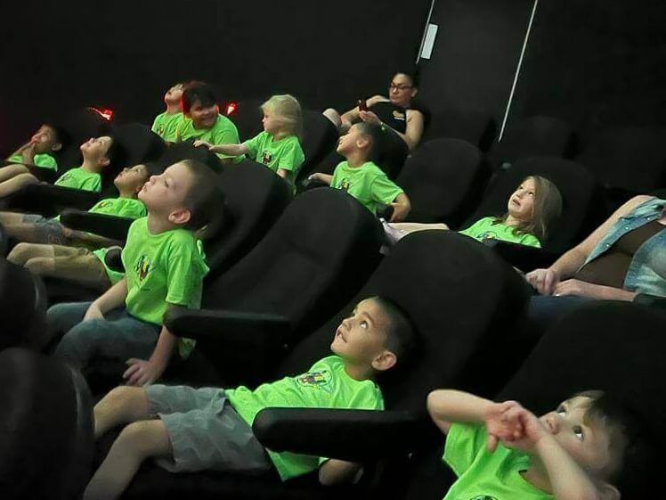 A group of children in green shirts are watching a movie