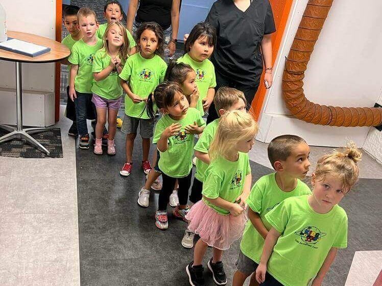 A group of children wearing green shirts are walking down a hallway.