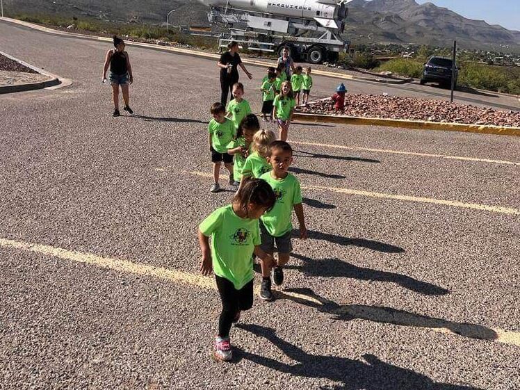 A group of children in green shirts are walking down a road.