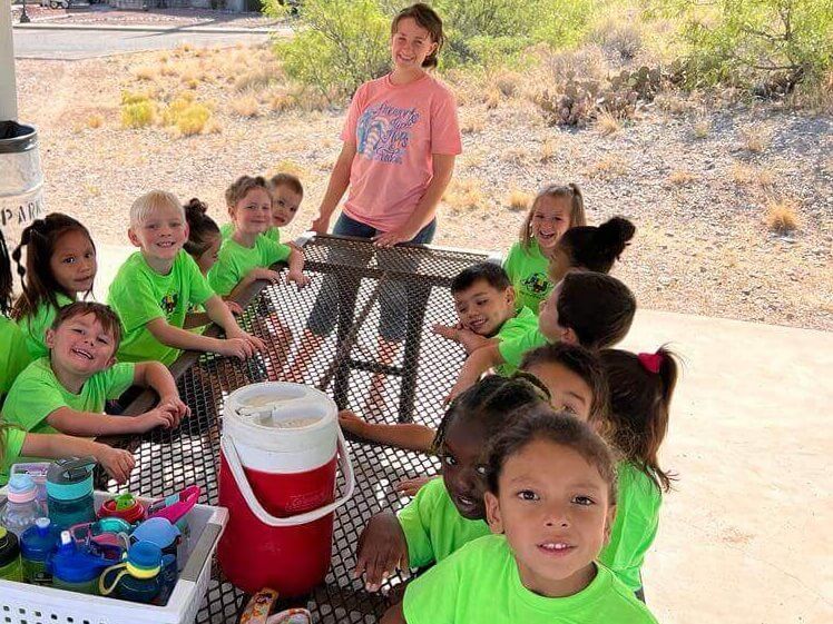 A group of children in green shirts are sitting at a picnic table