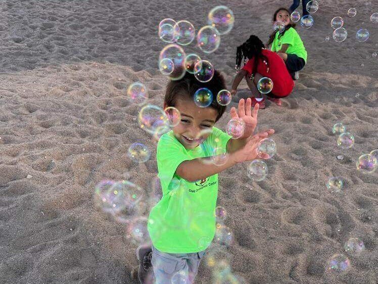 A young boy is playing with soap bubbles on the beach.