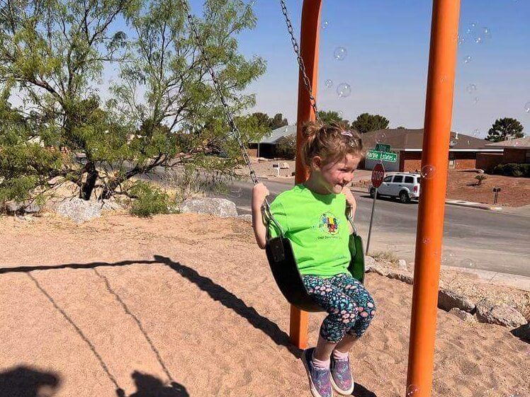A little girl in a green shirt is sitting on a swing.