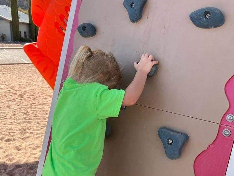 A little girl in a green shirt is climbing a climbing wall