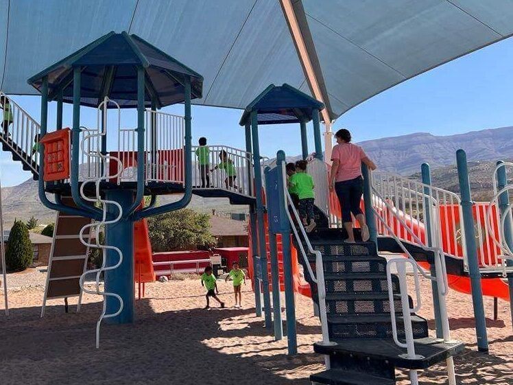 A group of children are playing on a playground with mountains in the background.