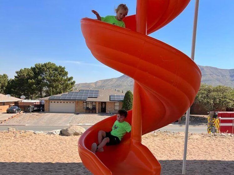 Two children are playing on an orange spiral slide