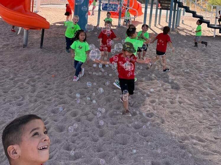 A group of children are playing with soap bubbles at a playground.