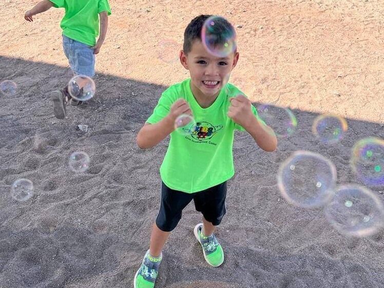 A young boy in a green shirt is playing with soap bubbles.