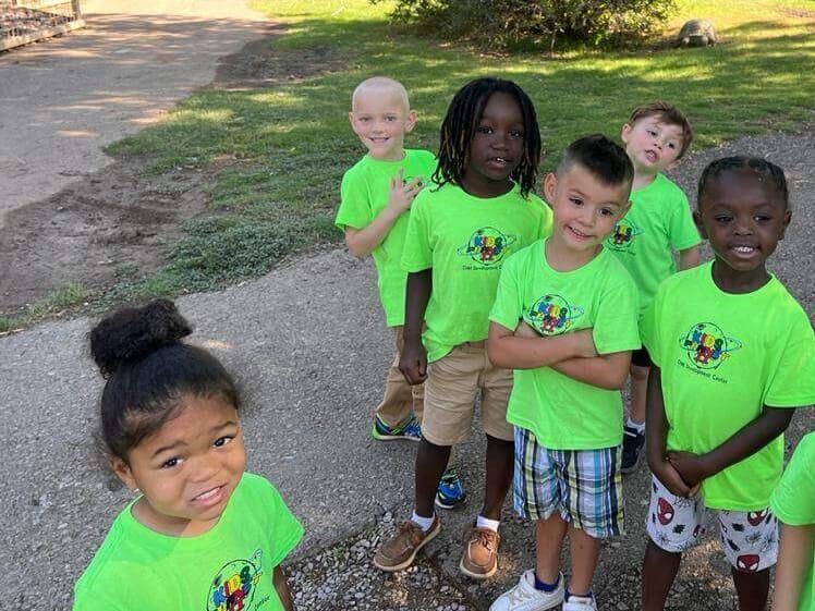 A group of children wearing green shirts are standing next to each other on a dirt road.