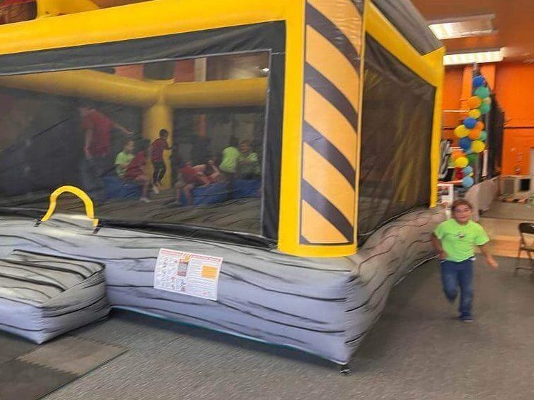 A boy in a green shirt is running in front of a bouncy house.