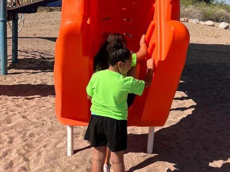 A little girl in a green shirt is playing on an orange slide