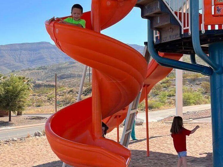 A boy and a girl are playing on an orange spiral slide at a playground.