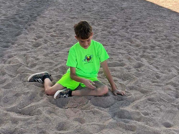A young boy in a neon green shirt is playing in the sand.