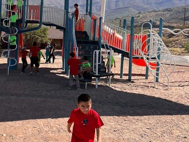 A boy in a red shirt stands in front of a playground