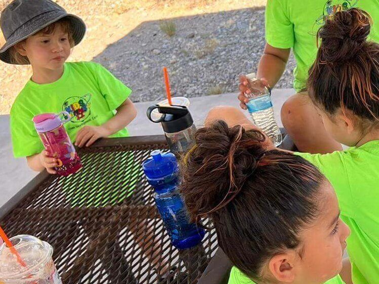 A group of children are sitting at a table with drinks and water bottles.
