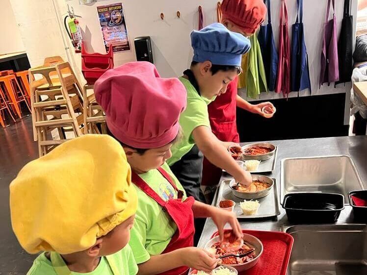 A group of children wearing chef hats and aprons are preparing food in a kitchen.