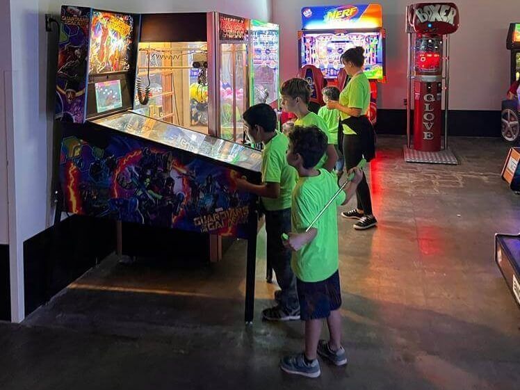 A group of children are playing a pinball machine in an amusement park.