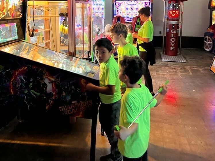 A group of young boys are playing pinball in an arcade.