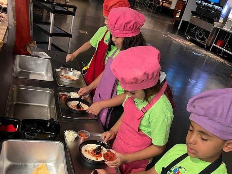 A group of children wearing chef hats and aprons are preparing food.