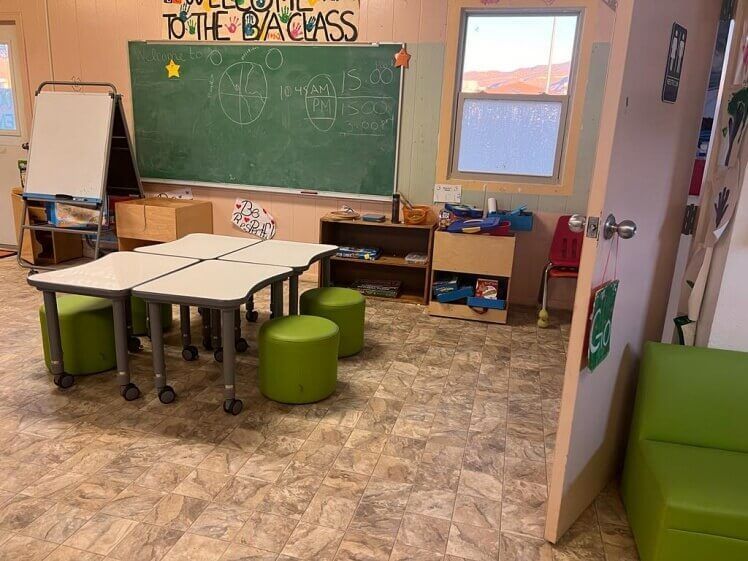 A classroom with tables and ottomans and a blackboard that says `` welcome back class ''.