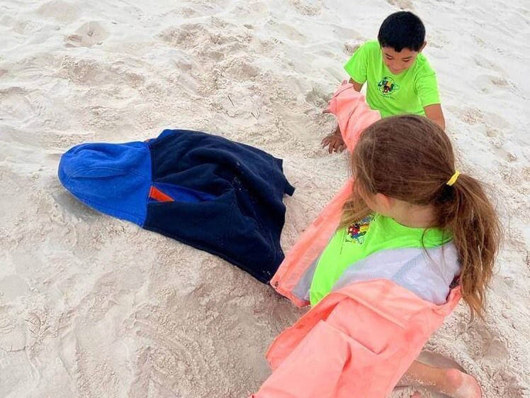 A boy and a girl are playing in the sand with towels.