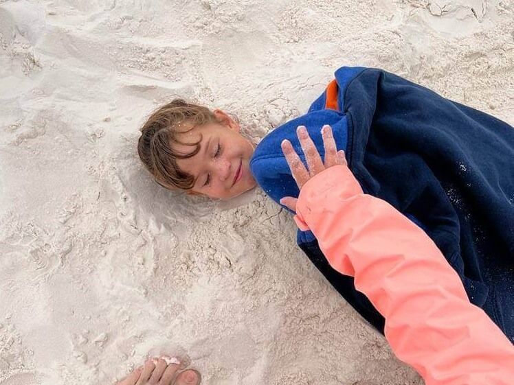 A child is wrapped in a towel and laying in the sand.